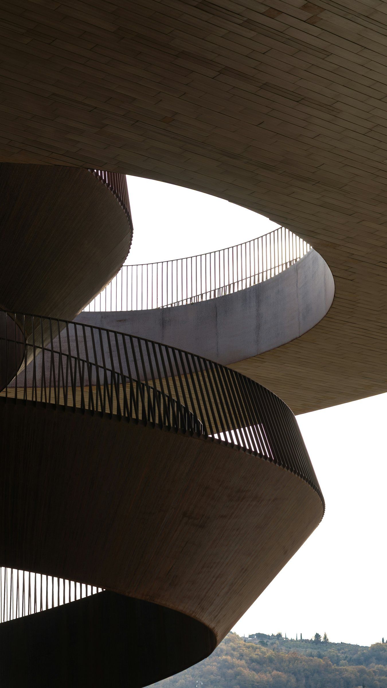 A curving timber staircase spiralling beneath an oculus of sky
